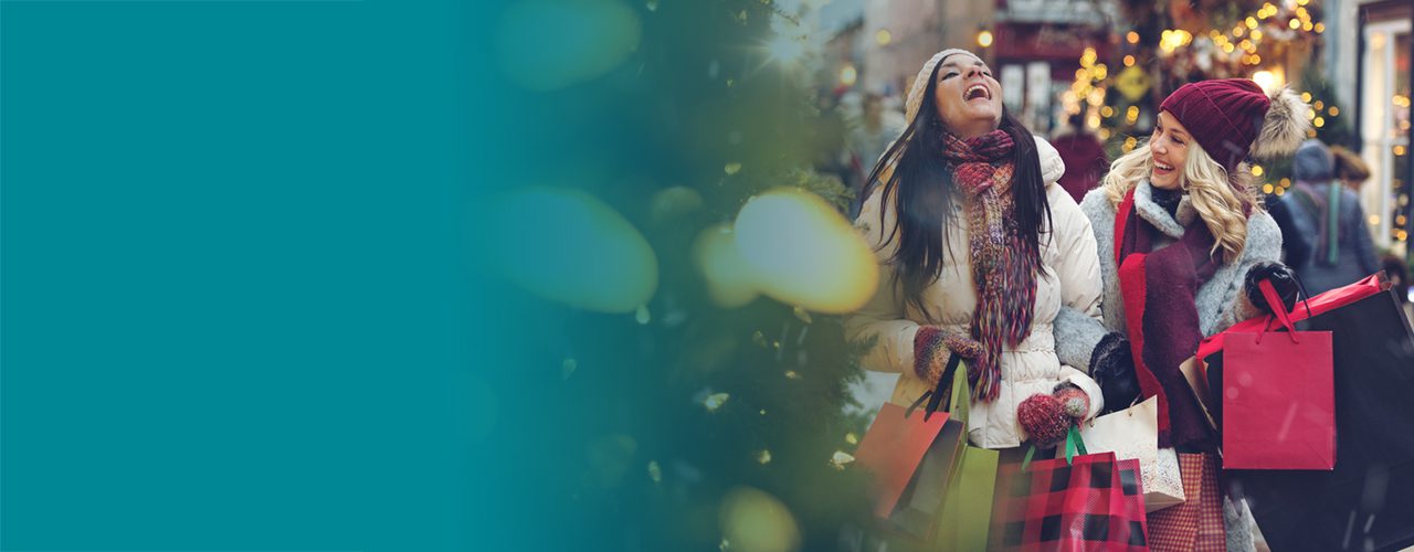 Two happy women with shopping bags walking outdoors during the holiday season.
